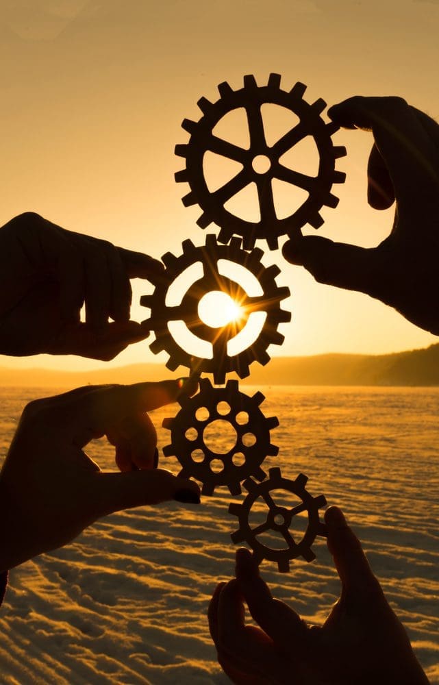 Four,Hands,Are,Holding,The,Gears,Against,The,Sunset.,Teamwork.