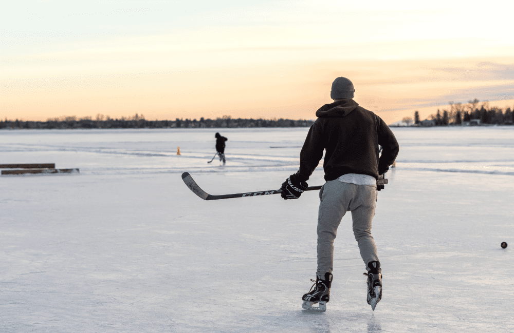 A man skating on the lake is seen with a hockey stick in hand