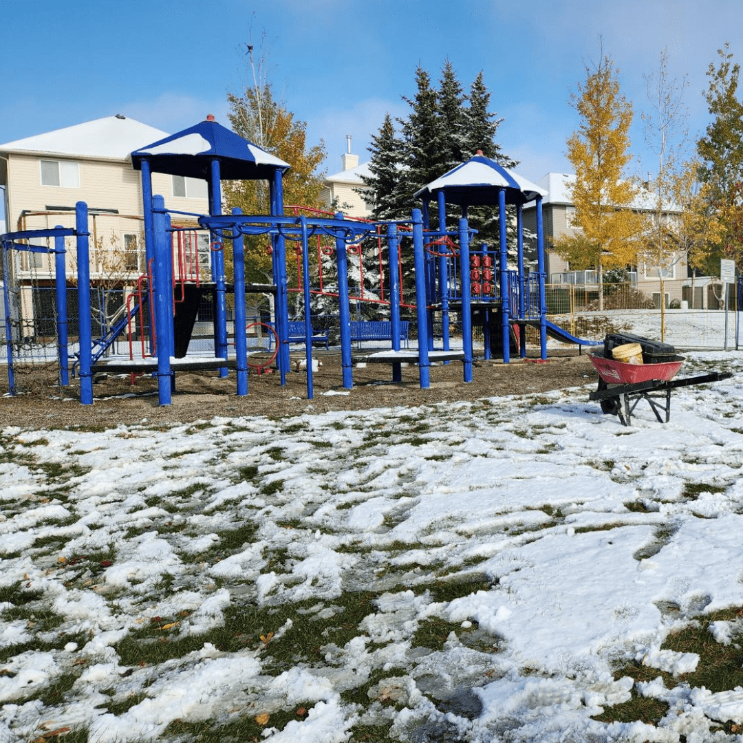 A photograph of the Hawkmere Playground. Equipment has been removed and a wheelbarrow can be seen beside the playground