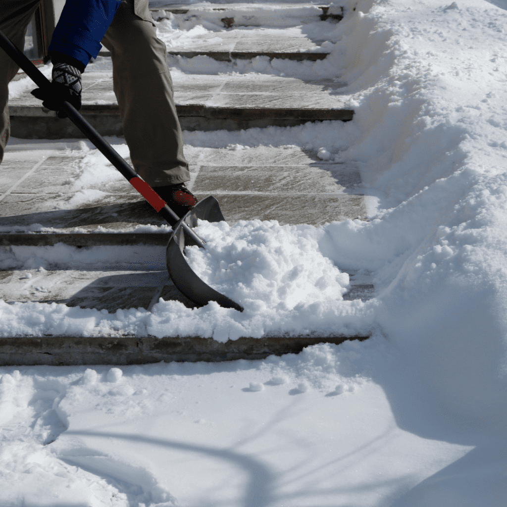 A close up of a shovel moving snow from a sidewalk.