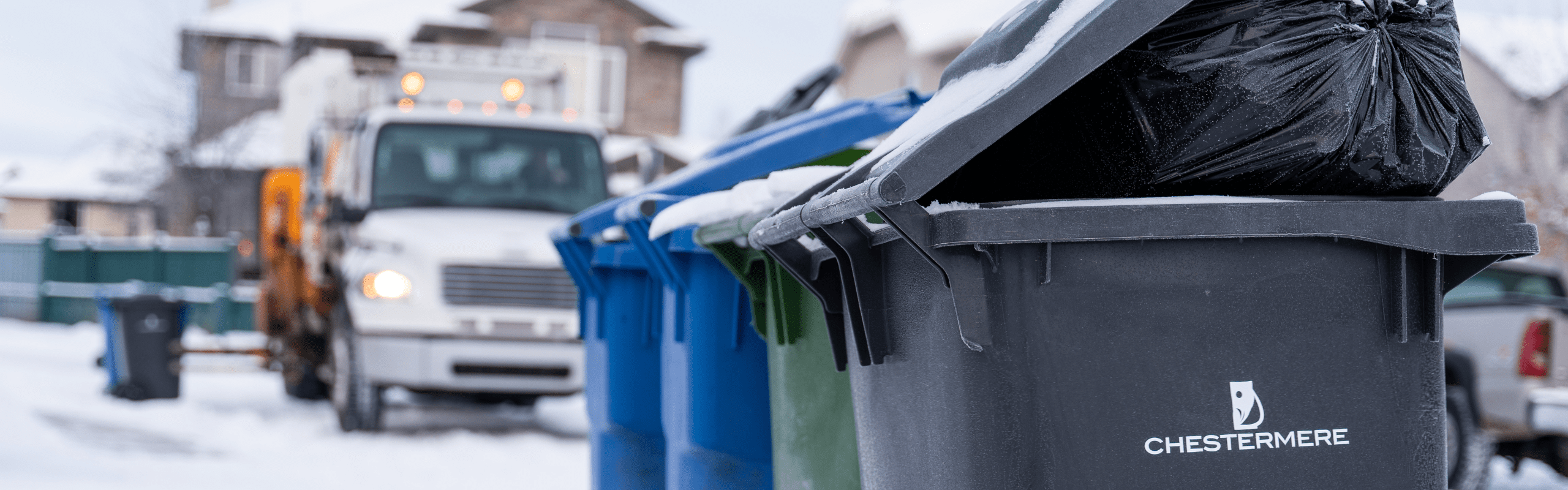 Coloured trash bins sit in the foreground with a garbage truck in the background. The Chestermere logo is visible on the bins.