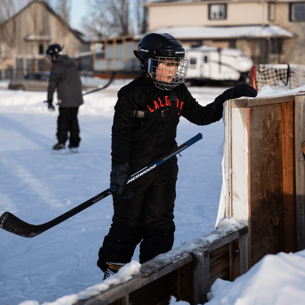 An exhausted hockey player catches his breath while leaning on the boards of a local outdoor rink