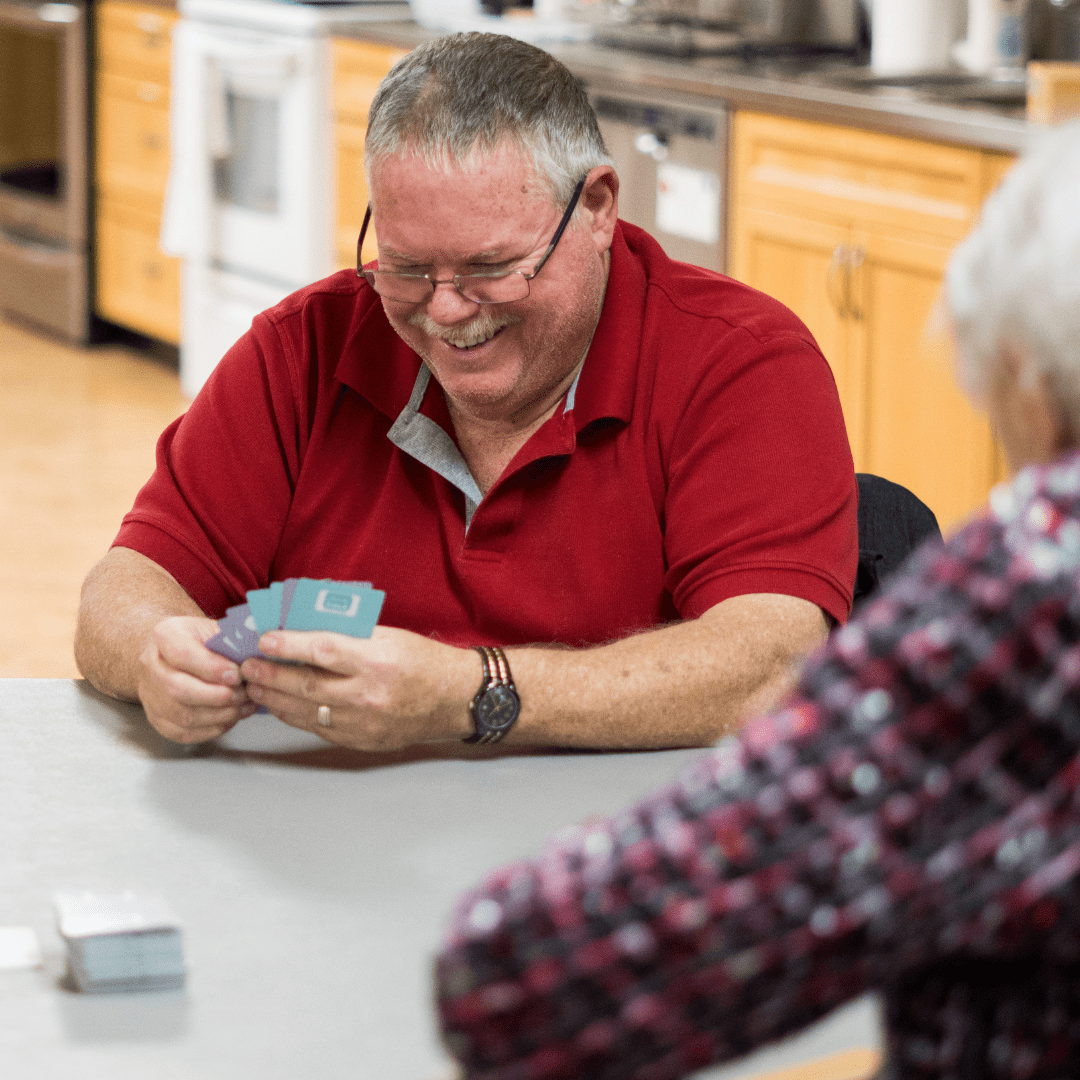 A man smiles while playing cards at a table.