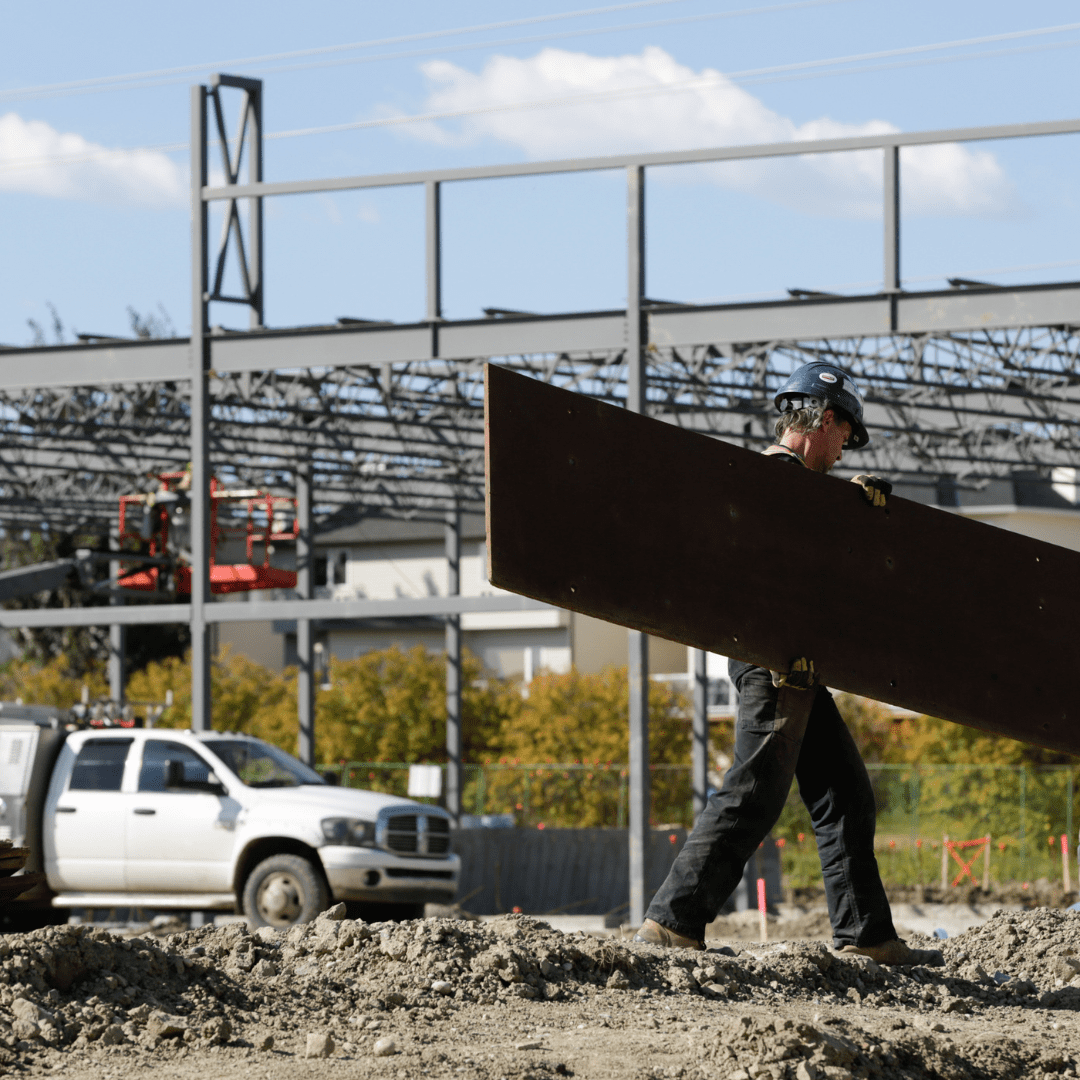 A construction worker is seen carrying a large piece of material on a construction site